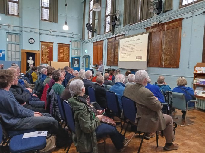 A hall full of people looking at a man presenting a talk